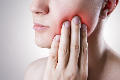 a close up view of a man touching his face, with a red glow from his cheek indicating that he has toothache