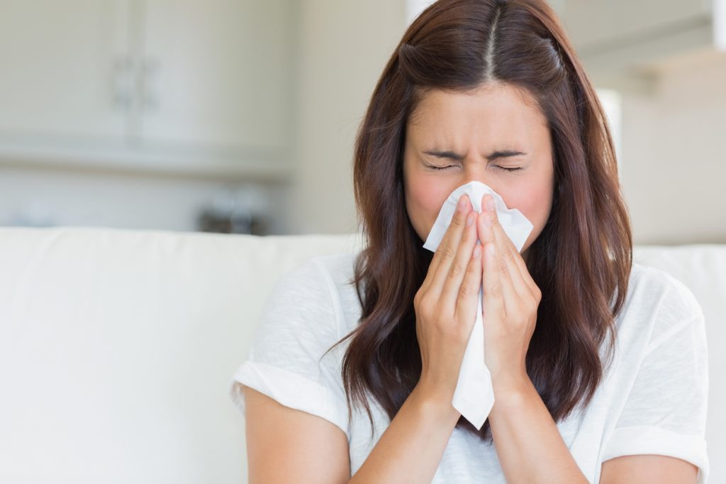 Brunette woman sneezing in a tissue in the living room