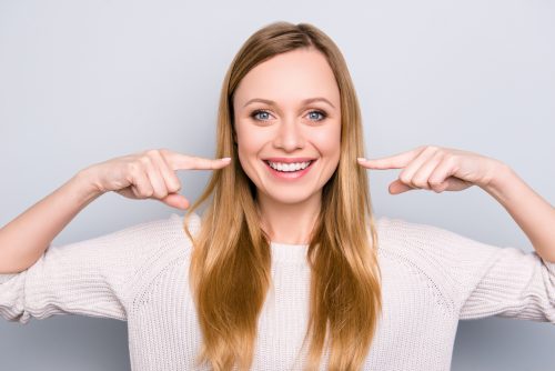 A smiling woman pointing at her teeth