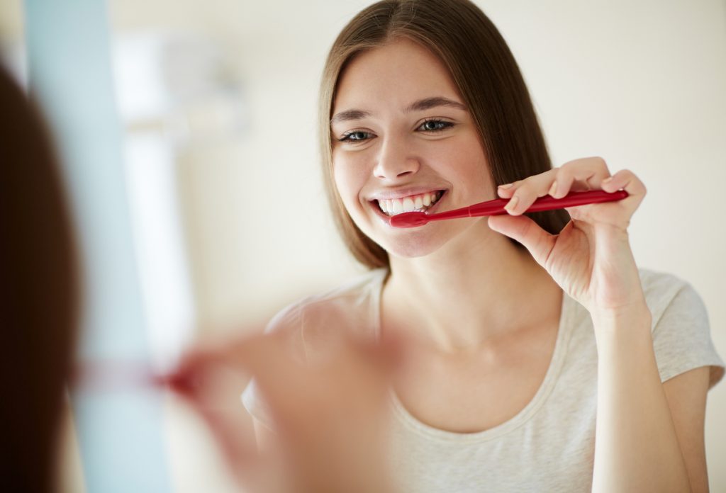 a young woman brushing her teeth at mirror