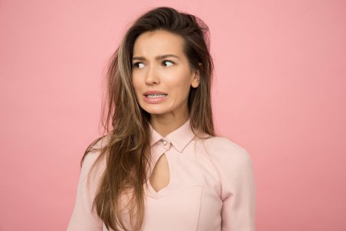 a young woman wearing a pink blouse looking scared