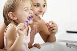 mother and daughter brushing teeth together in front of a mirror