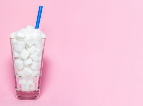 A glass full of sugar cubes with a blue straw and a pink background